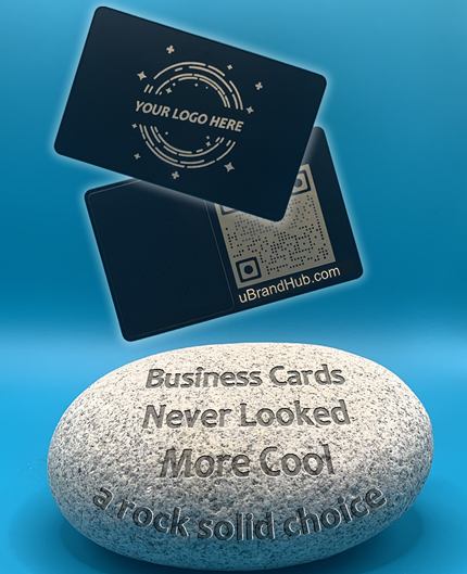 Black metal NFC card with front and back views. The front features the words 'Your Logo Here' while the back displays a laser-engraved QR code with a gold undertone. The card is depicted hovering over a rock engraved with 'A rock solid choice' and 'Business Cards Never Looked More Cool.' The background is blue with a page curl in the upper right corner revealing the text 'Included with every purchase,' indicating that an NFC card is included with the purchase of uBrand Hub service.