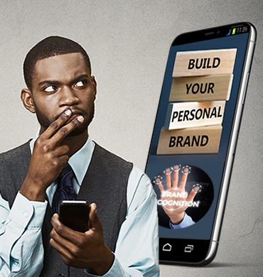 African American male holding a cellphone in his left hand, with two fingers over his lips from his right hand. His eyes are focused slightly upward over his left shoulder, appearing to contemplate the content on his phone. Over his shoulder, there's a view of a mobile phone displaying four rectangular building blocks stacked on top of each other, with words in descending order: 'Build', 'Your', 'Personal', 'Brand'.